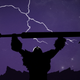 A character from the animated film The Spire of Night, raising his sword to the air as lightning strikes.
